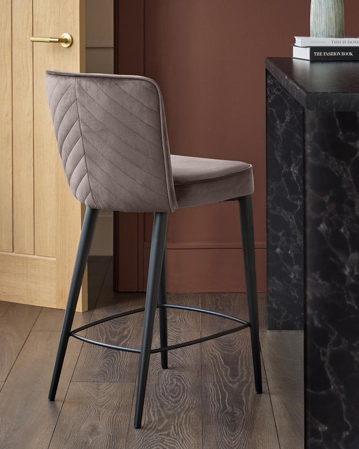 Serena Velvet Bar Stool in Mocha, shown from rear angle with quilted backrest, black metal legs and footrest on wood flooring.