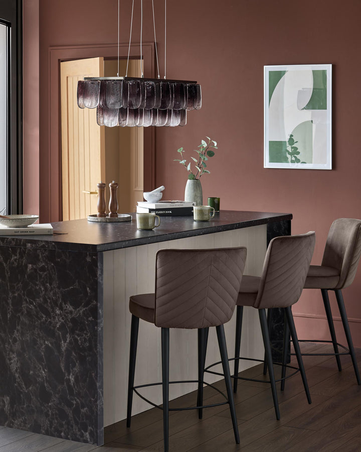 Mocha velvet bar stool with quilted backrest and black metal legs, shown at kitchen island.