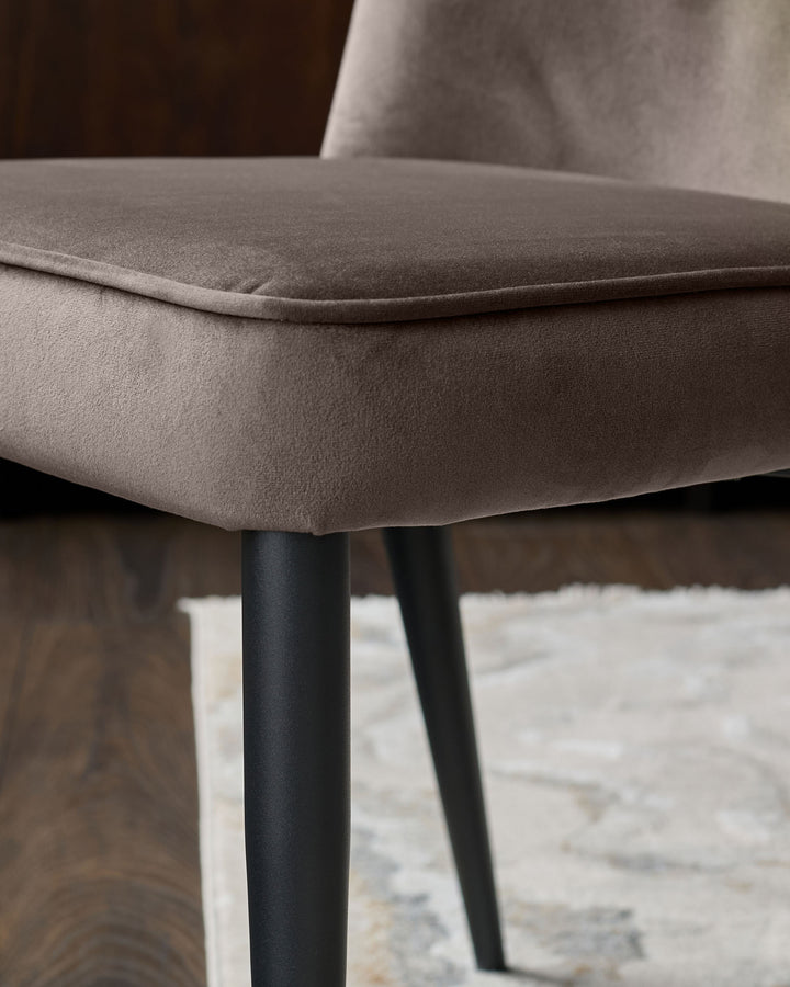 Serena velvet dining chair in mocha, side view showing curved seat cushion and black tapered legs on area rug.