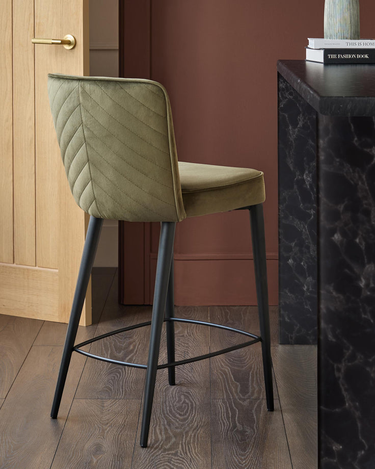 Stylish green velvet bar stool with black legs and footrest, positioned next to a marble countertop for a contemporary look.