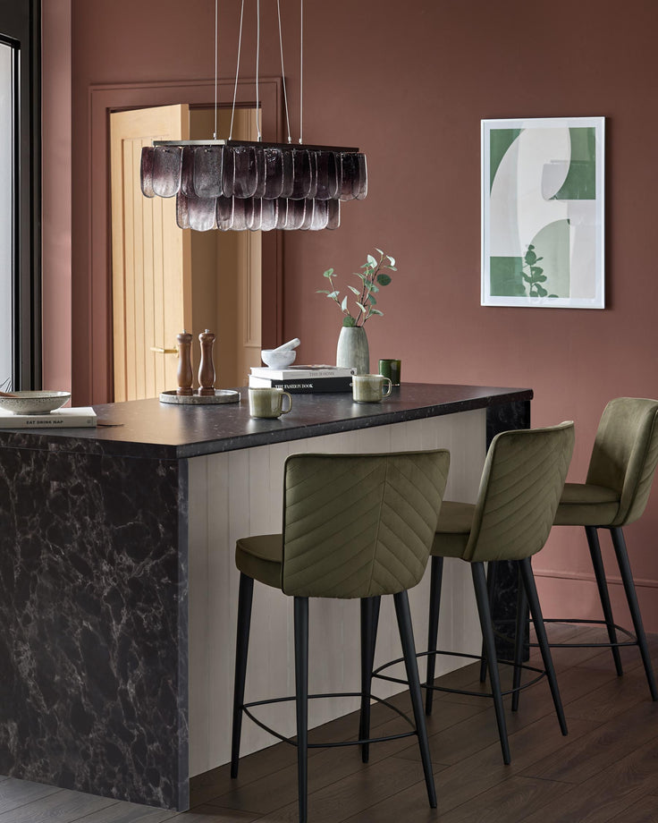 Kitchen island with three olive green bar stools, black marble countertop and modern pendant lighting.