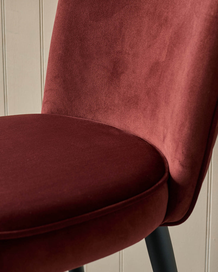 Close-up of a stylish, red velvet chair, showcasing its plush fabric and modern design against a neutral backdrop.