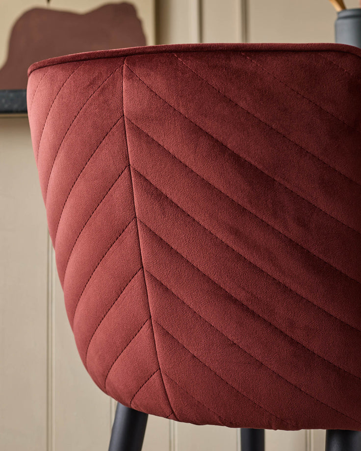 Close-up of a stylish, quilted, burgundy velvet chair, showcasing its texture and design.