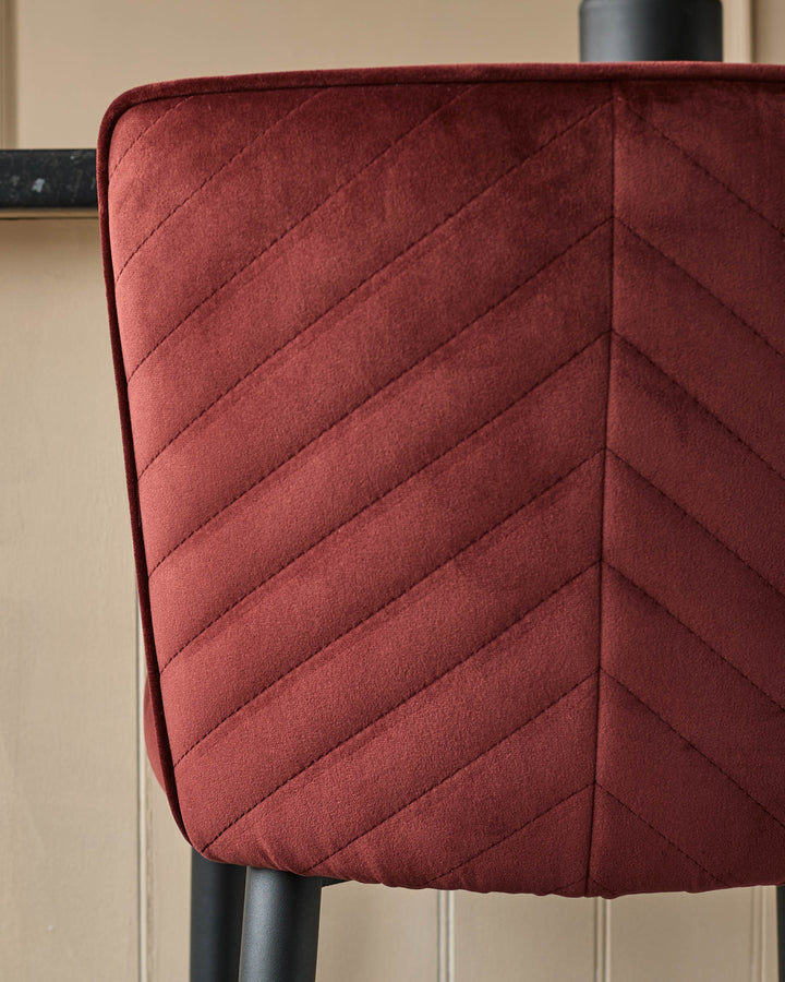 Close-up of a stylish, quilted, dark-red chair back with black legs. A modern and comfortable design.