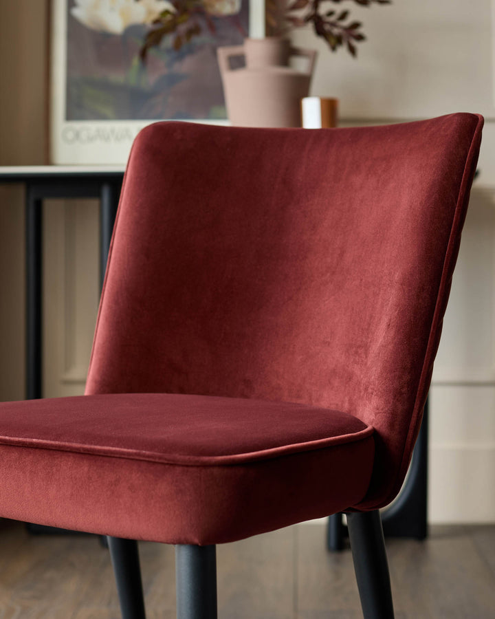 Close-up of a stylish velvet chair in a rich, dark red, with sleek black legs, perfect for adding a touch of luxury to any dining space.
