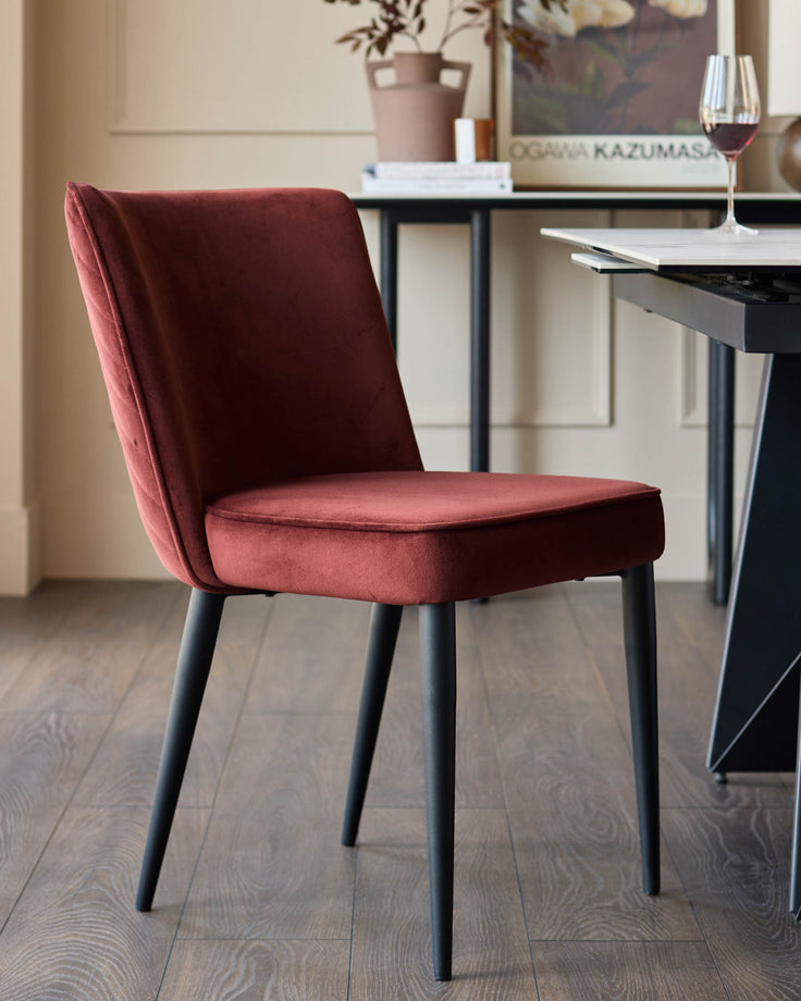 A luxurious-looking, dark red velvet dining chair with a sleek black metal frame, set within a stylish dining area.