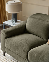 Dark green fabric armchair with curved backrest and armrests, paired with white side table and cream table lamp.