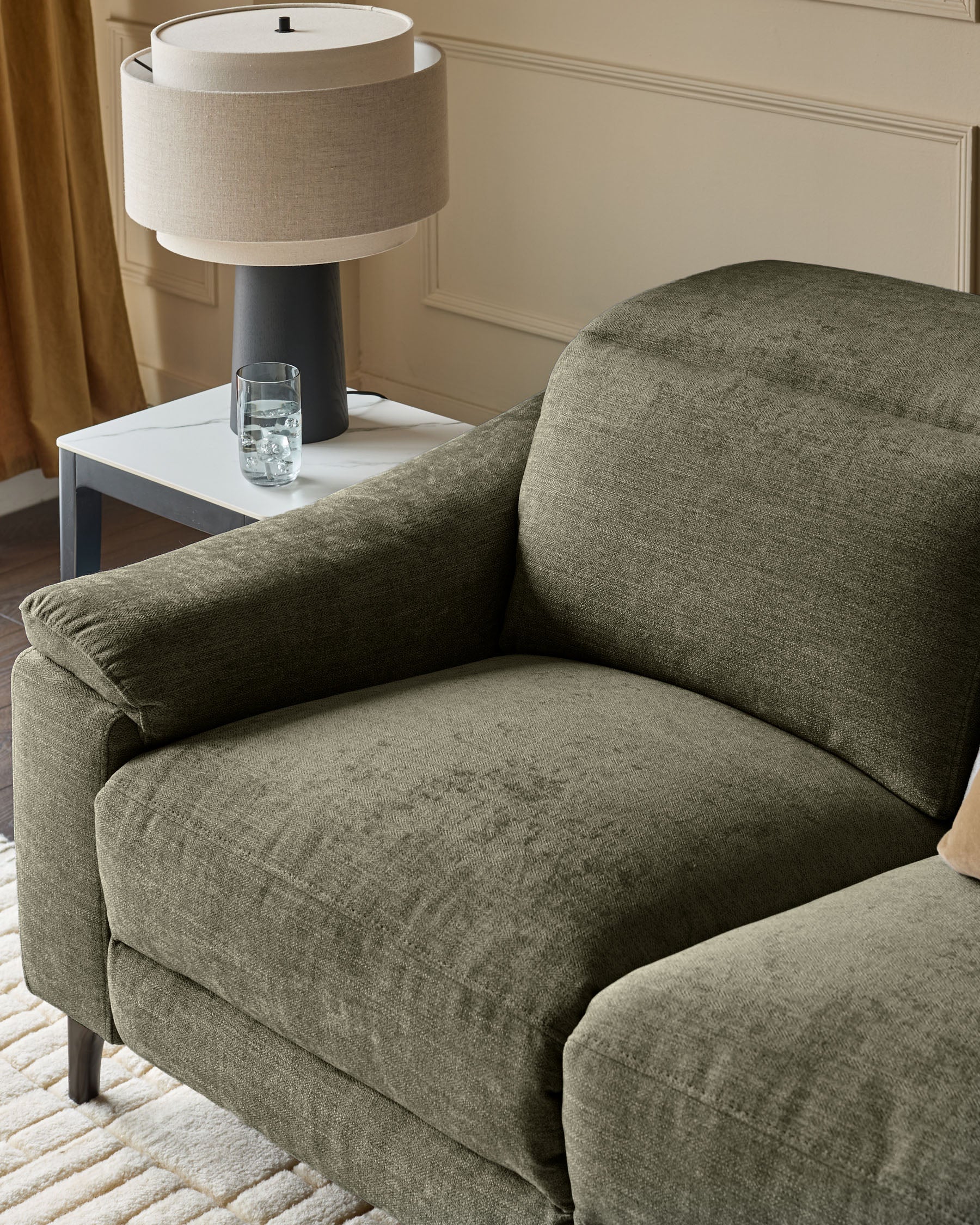 Dark green fabric armchair with curved backrest and armrests, paired with white side table and cream table lamp.