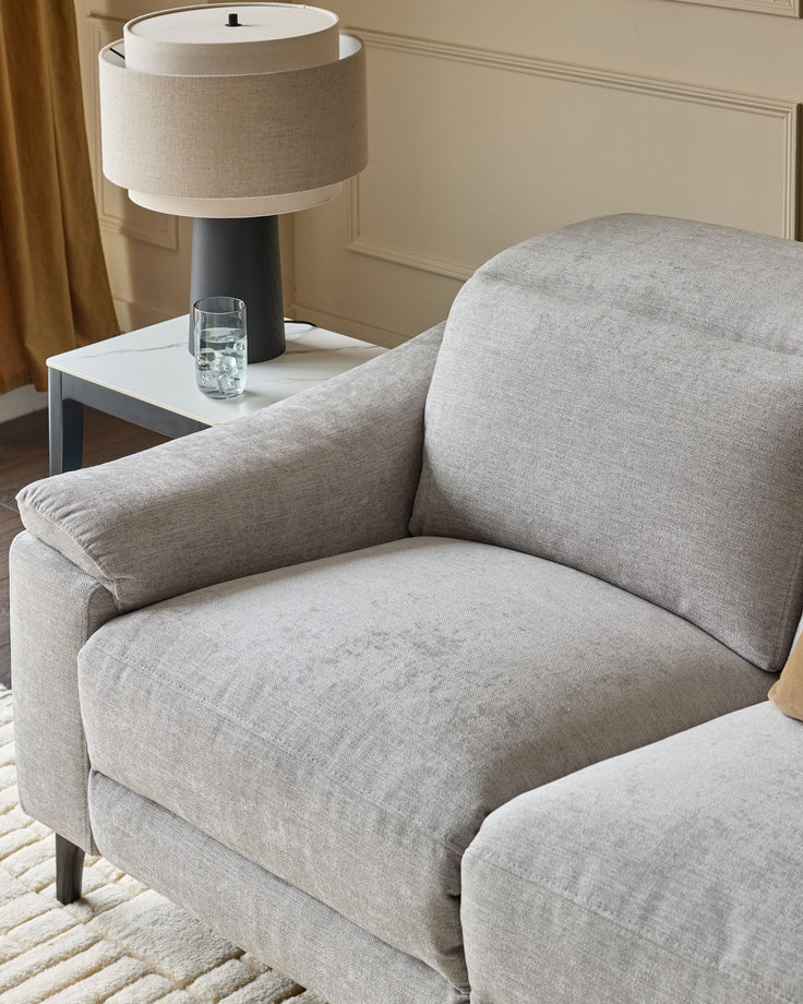 Light grey fabric 2-seater recliner sofa with curved arms and cushioned backrest in modern living room setting.
