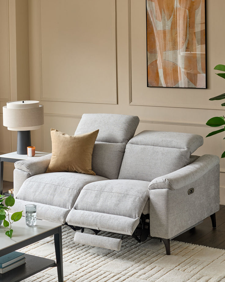 Serene 2-seater light grey fabric recliner sofa with footrests extended, paired with gold cushion in modern living room setting.
