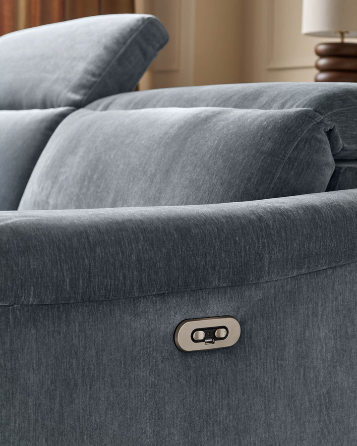 Gray fabric recliner sofa corner section with visible control button and throw pillows in neutral bedroom setting.