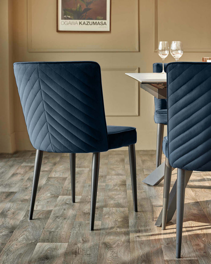 Close-up of a navy velvet dining chair with a chevron pattern back and dark metal legs. Table and glasses are partially visible.