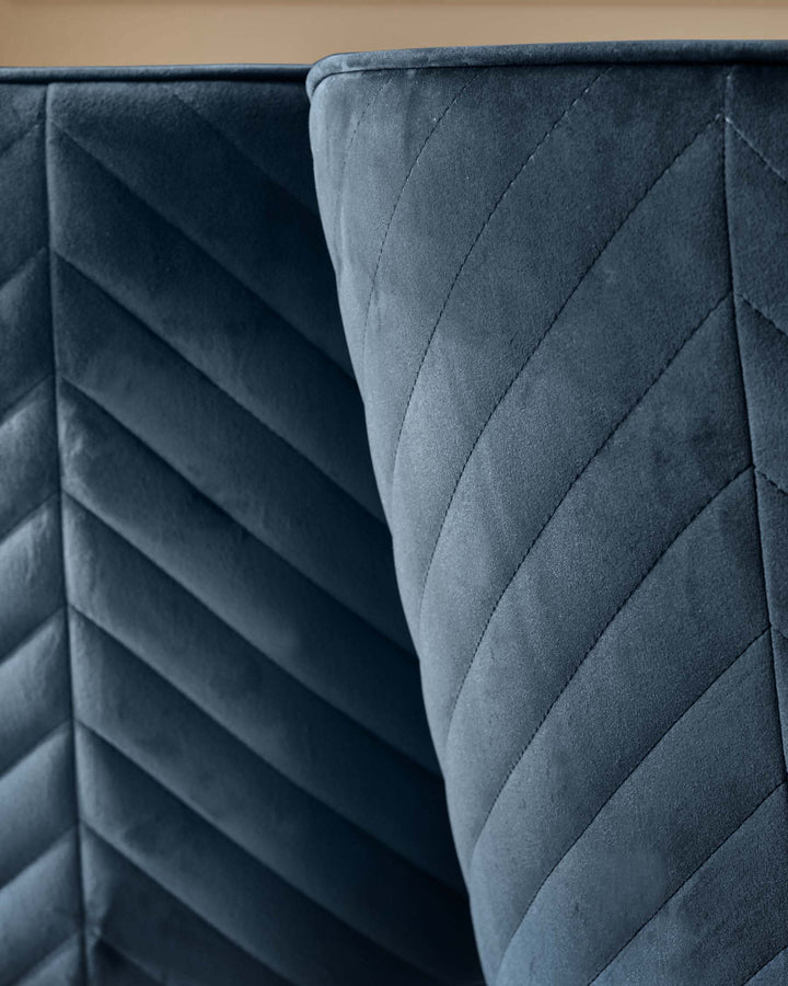 Close-up of a blue, quilted fabric sofa or headboard, showcasing its texture and detailed stitching.
