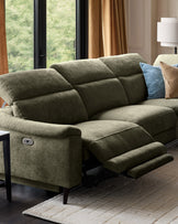 Dark green chenille right chaise recliner sofa with extended footrest, shown in living room with decorative pillows and large windows.