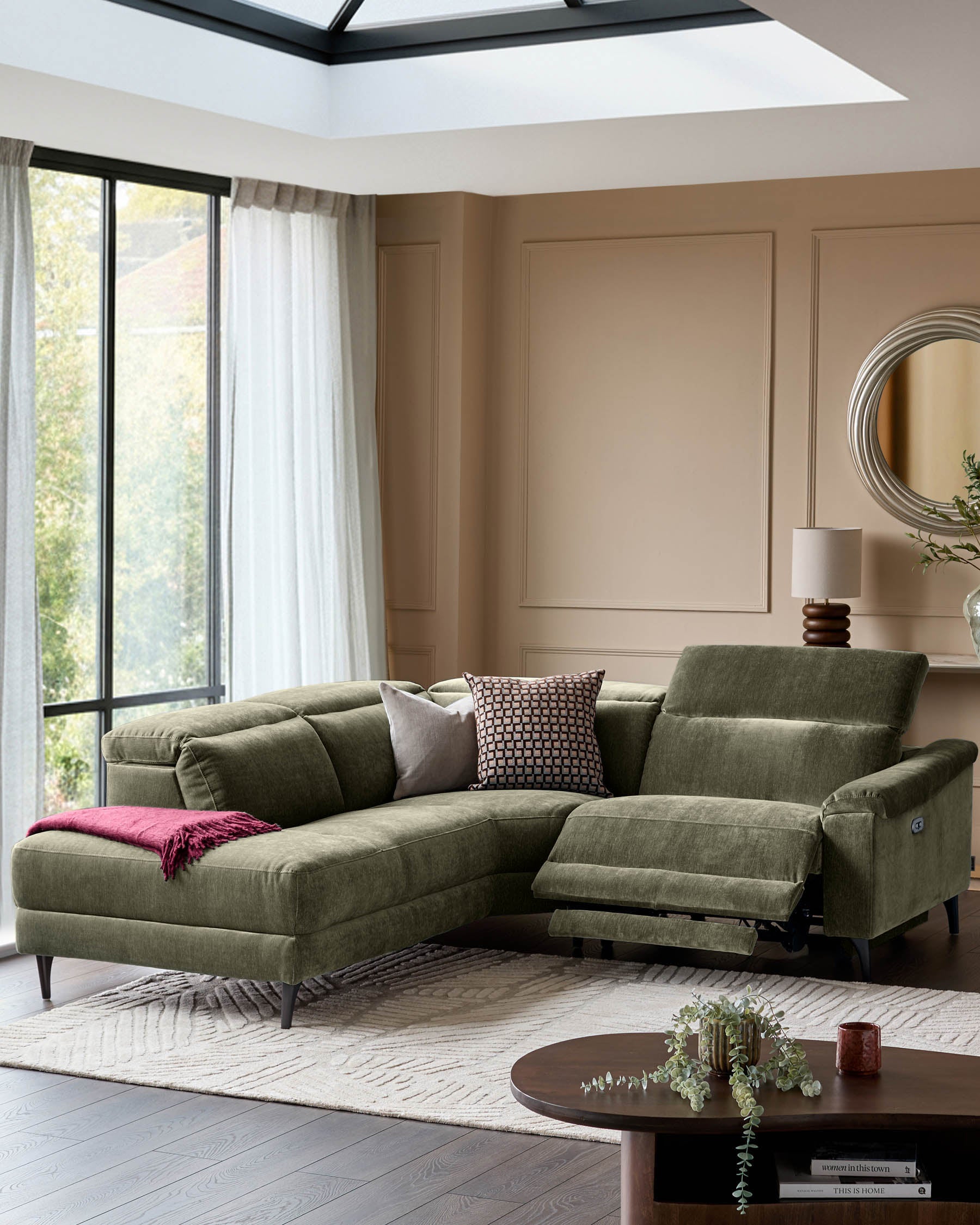 Serene left small corner recliner sofa in dark green fabric with footrest extended, positioned in a bright living room.