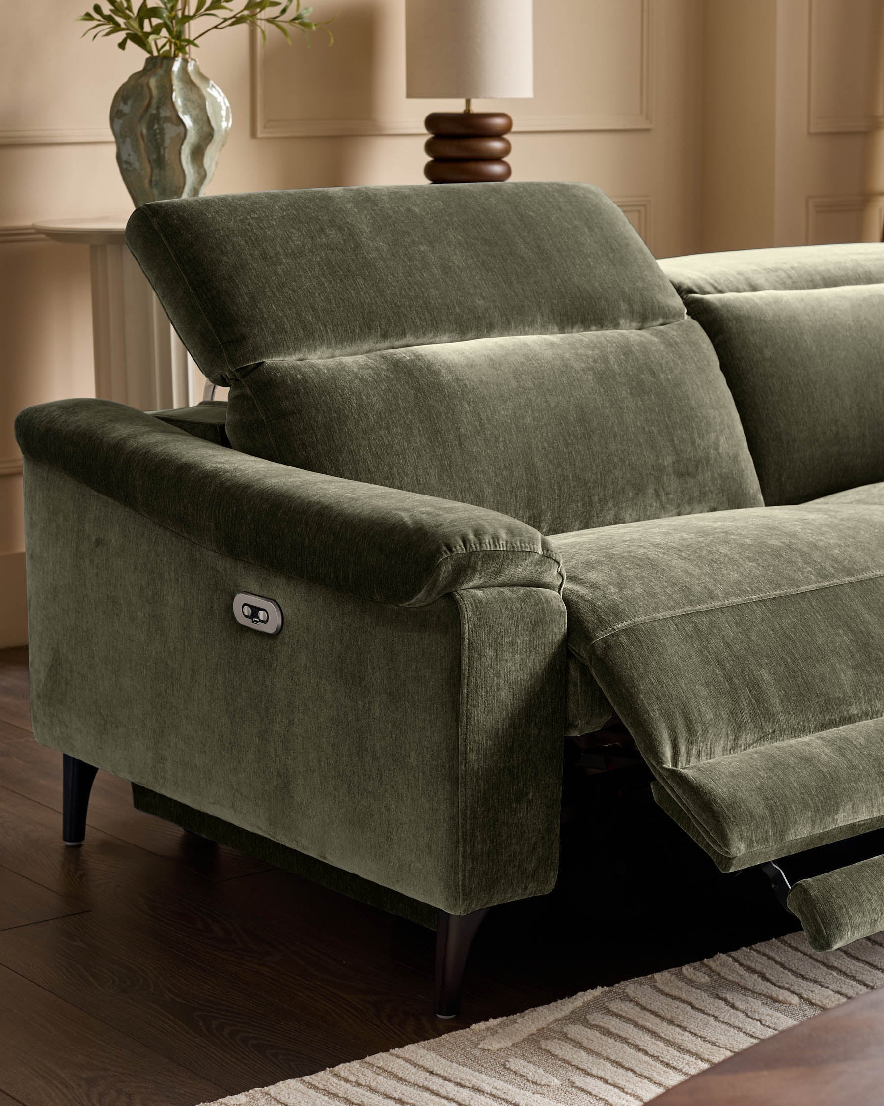 Dark green fabric reclining corner sofa with extended footrest, showing white control button on armrest, dark wooden legs.