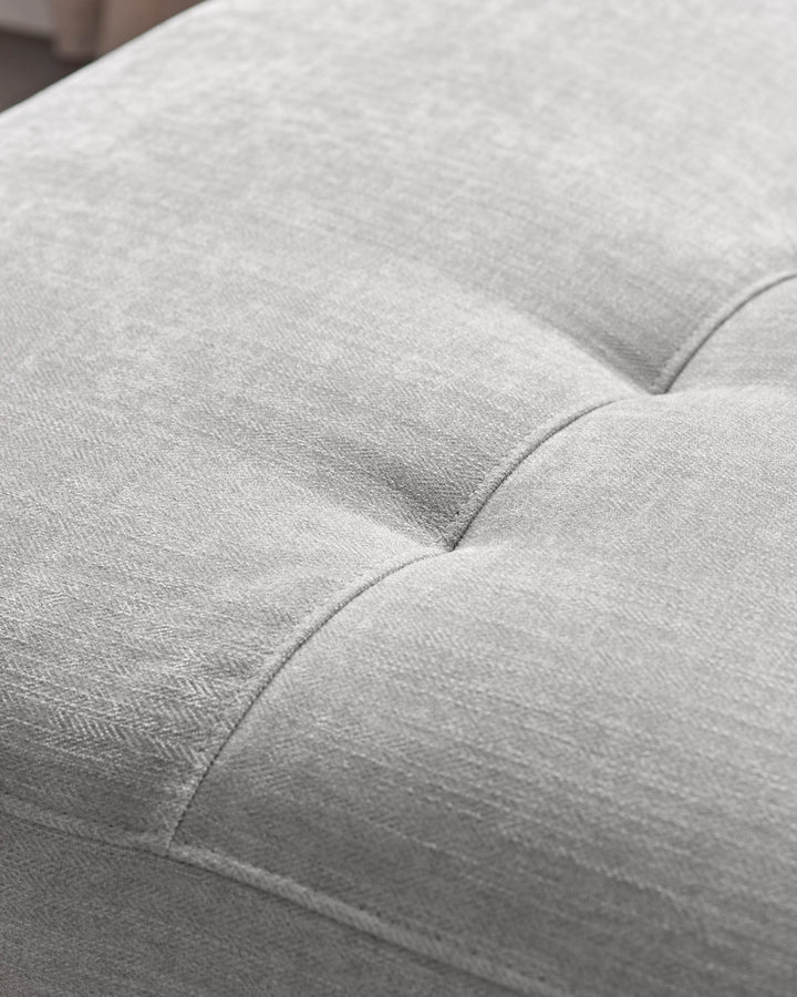 Close-up of light grey fabric on a recliner sofa, showing quilted seating with subtle texture and stitched details.