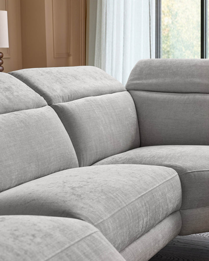 Light grey fabric right-hand corner recliner sofa with curved cushioned sections and padded armrests, shown in modern bedroom setting.
