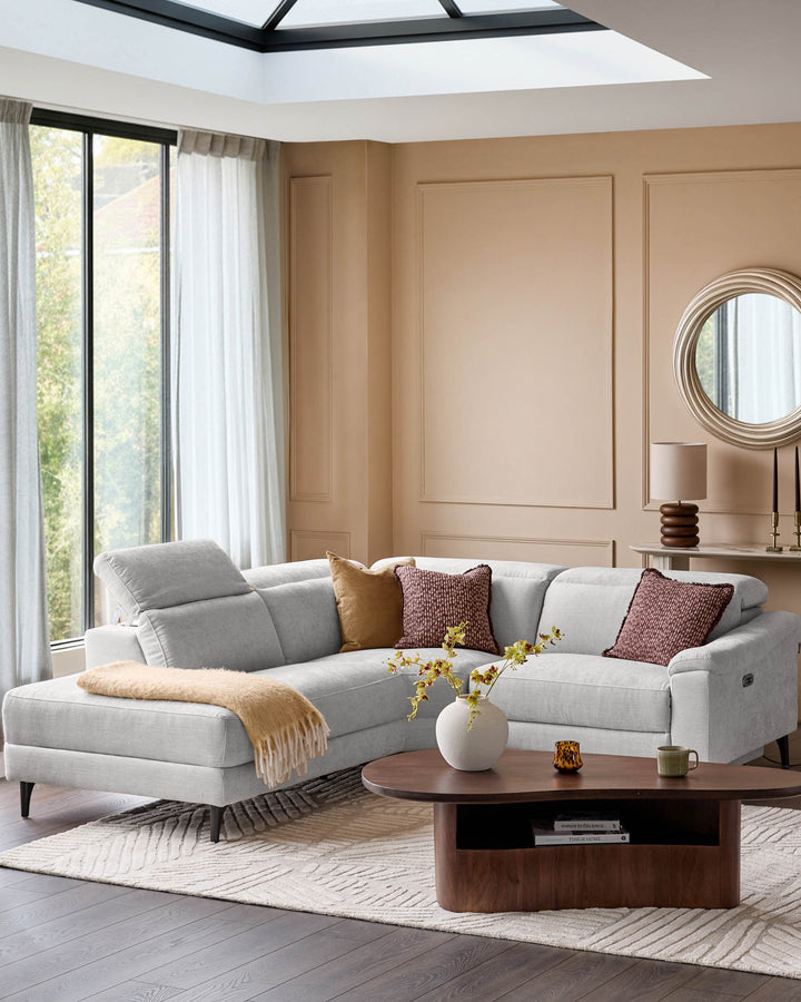 Light grey left-facing corner recliner sofa with curved design, positioned in a modern living room with warm beige walls and skylight.