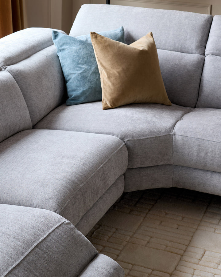 Serene left chaise recliner sofa in light grey chenille with blue and tan accent pillows, curved sectional design.