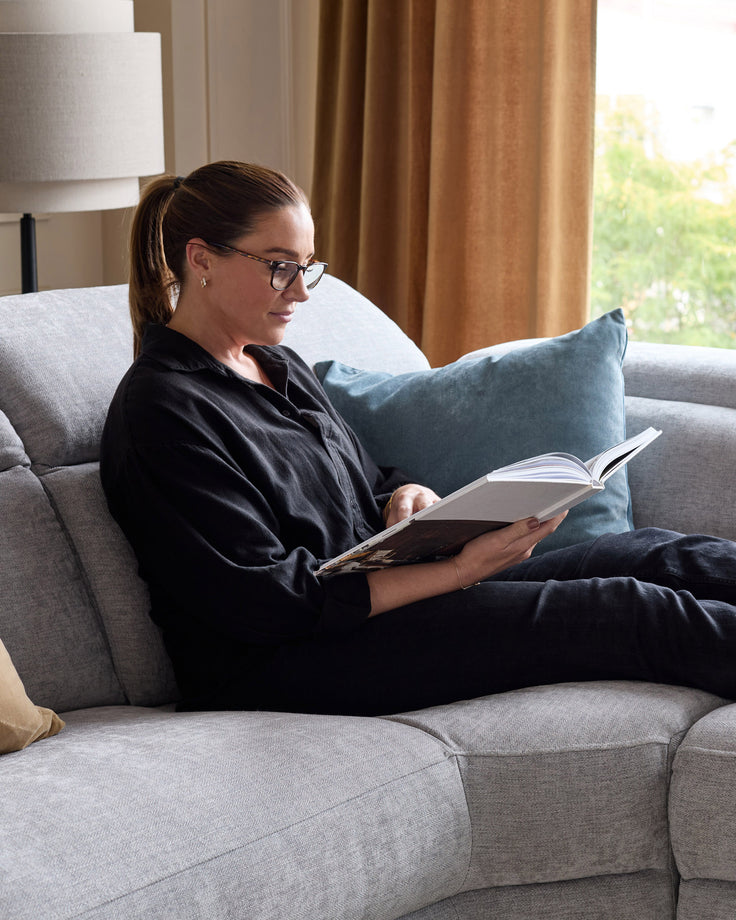 Light grey chenille left chaise recliner sofa with woman seated reading, featuring blue accent pillow.