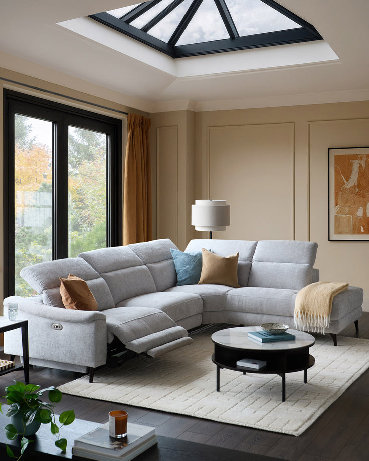 Light grey chenille right chaise recliner sofa in modern living room with skylight and black-framed glass doors.