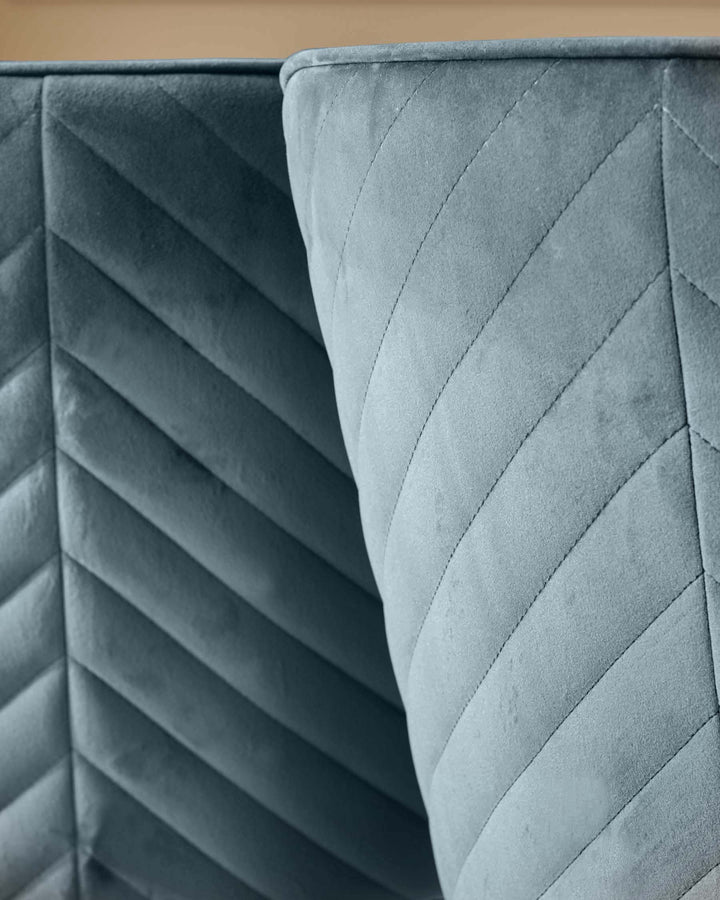 Close-up of a quilted blue sofa, showcasing the detailed stitching and plush texture of the fabric.