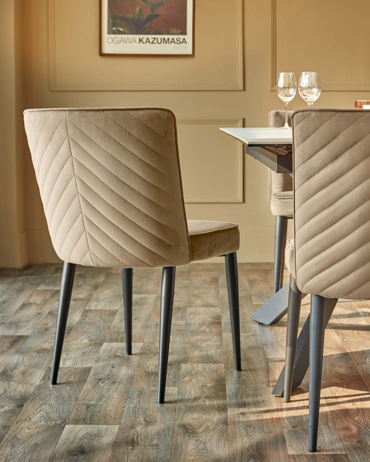 A beige dining set features soft, textured chairs with dark legs and a sleek, modern table in a well-lit dining space.