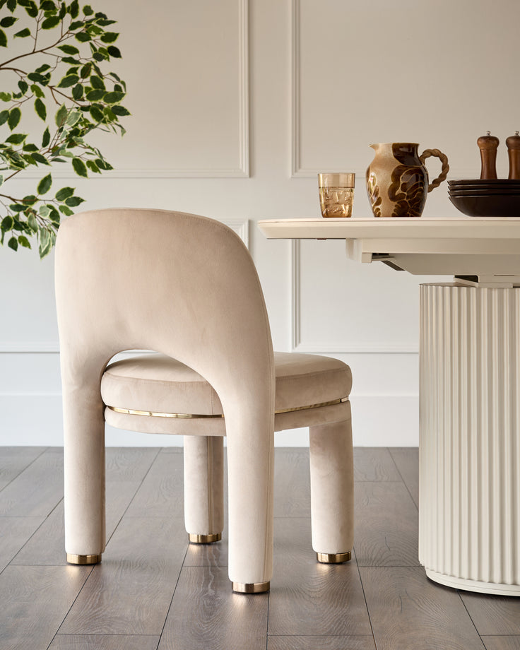 Shay dining chair in champagne velvet with curved backrest and brass leg caps, positioned at white desk.
