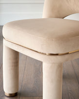 Shay dining chair in champagne velvet, shown at angle displaying curved seat, cylindrical legs with brass base detail.