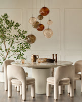 Shay dining chair in champagne velvet with curved back and cylindrical legs in a cream dining room setting.
