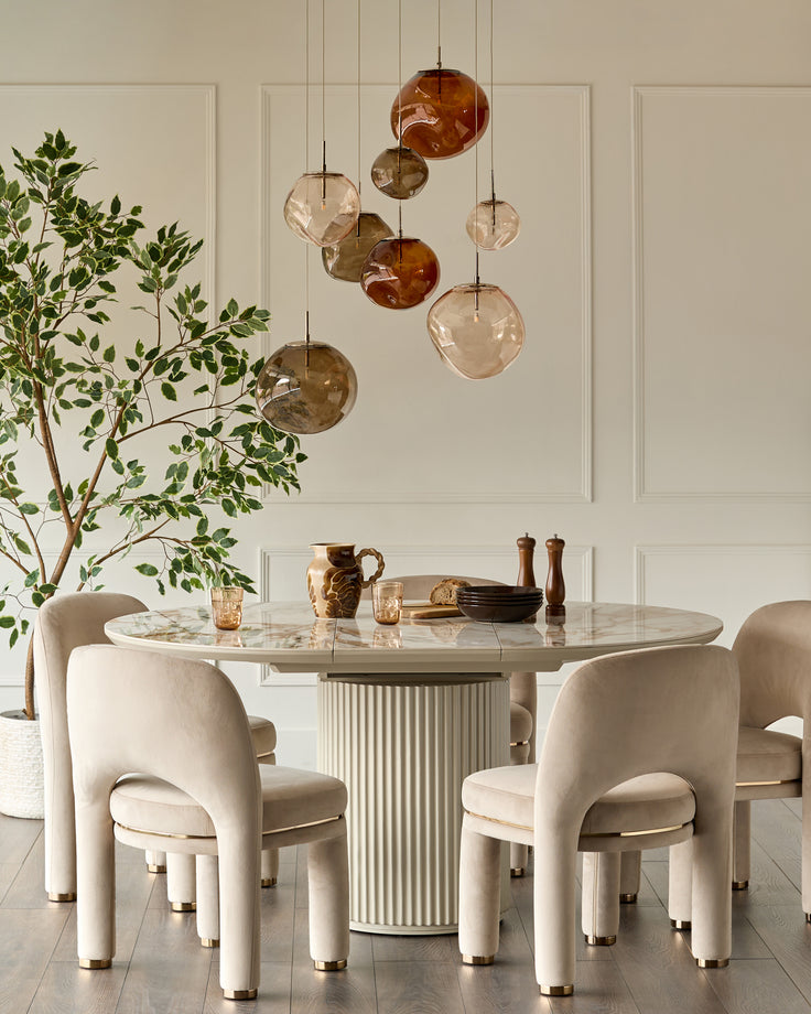 Shay dining chair in champagne velvet with curved back and cylindrical legs in a cream dining room setting.