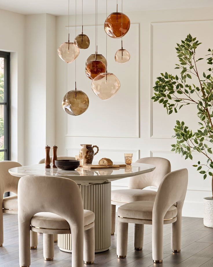 Shay dining chair in champagne velvet with curved backrest and brass feet, shown in dining room setting.