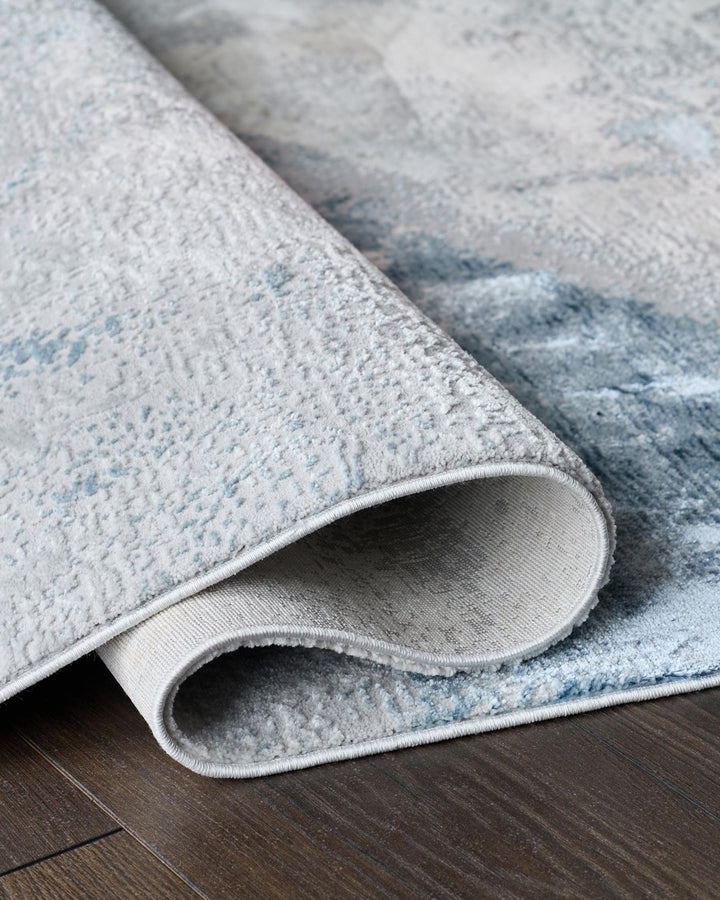 Rolled up light blue and grey rug on a dark wood floor. The rug has a subtle pattern.