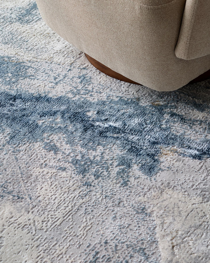 Close-up of a beige armchair resting on a textured rug with a blue abstract design. Elegant and comfortable furniture.