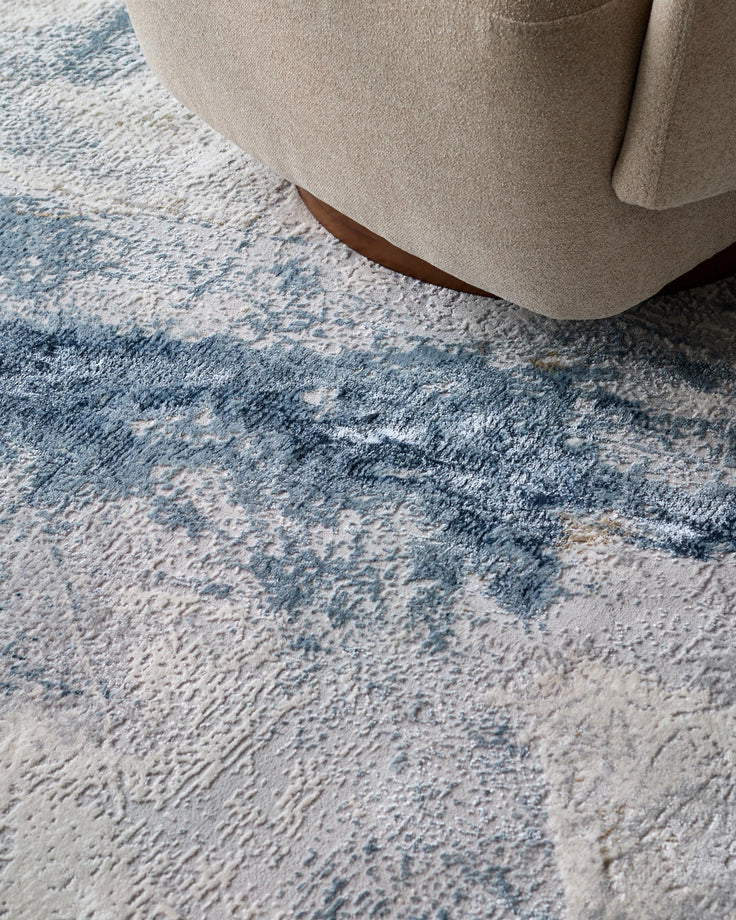 Close-up of a beige armchair resting on a textured rug with a blue abstract design. Elegant and comfortable furniture.