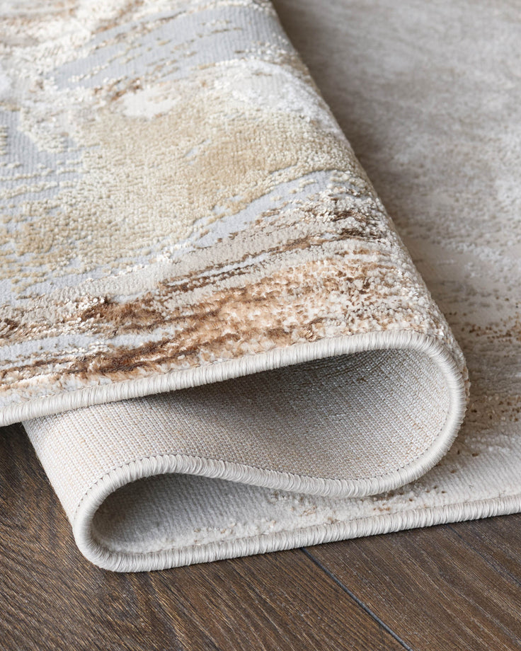 Close-up of a rolled, patterned rug showing the textured surface and backing on a wooden floor. Neutral colour palette.