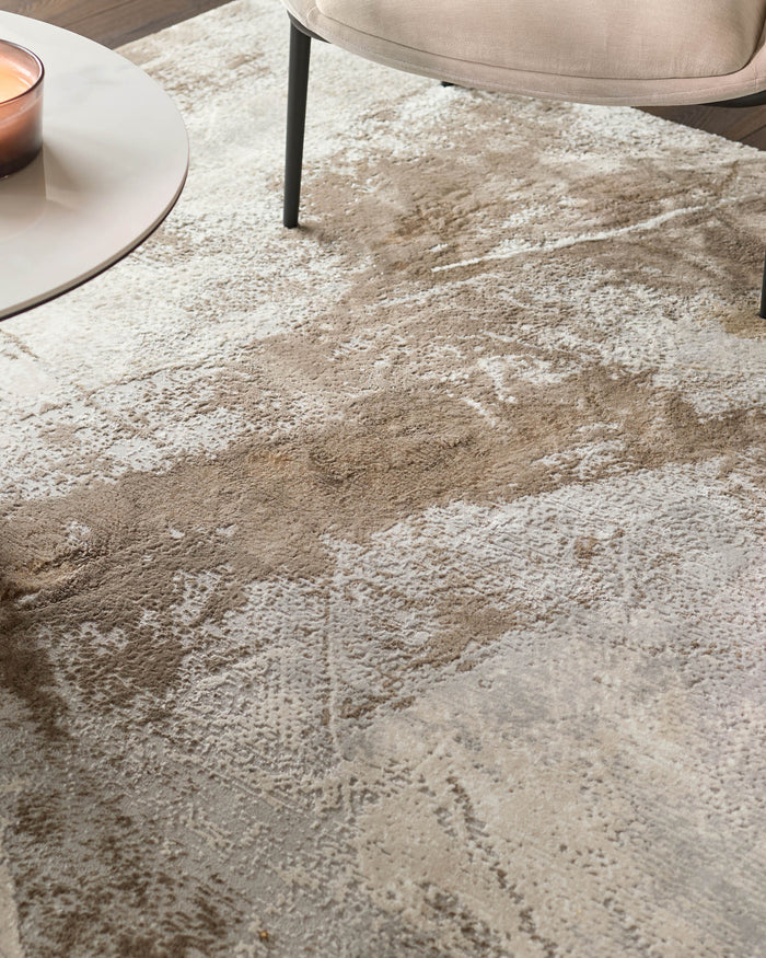 Close-up of a beige and cream patterned rug, with a round coffee table and chair legs visible.