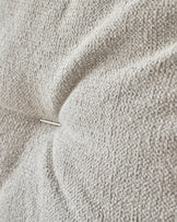 Close-up of textured, button-tufted upholstery in a neutral grey, featuring a visible pin for a detailed look.