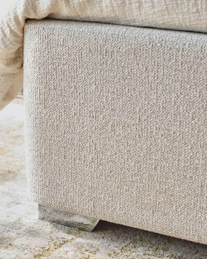 Close-up of an ottoman with textured fabric, complemented by a soft throw and patterned rug for a cosy interior look.