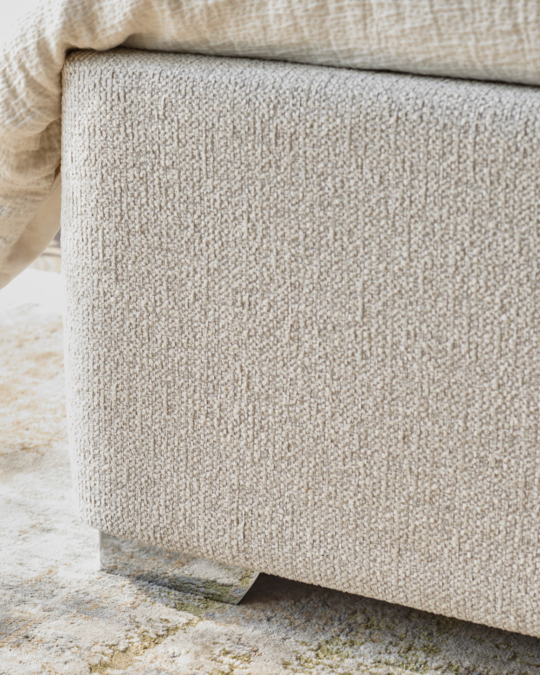 Close up of textured neutral storage bench with soft blanket and geometric rug, showcasing fabric detail and stylish design.