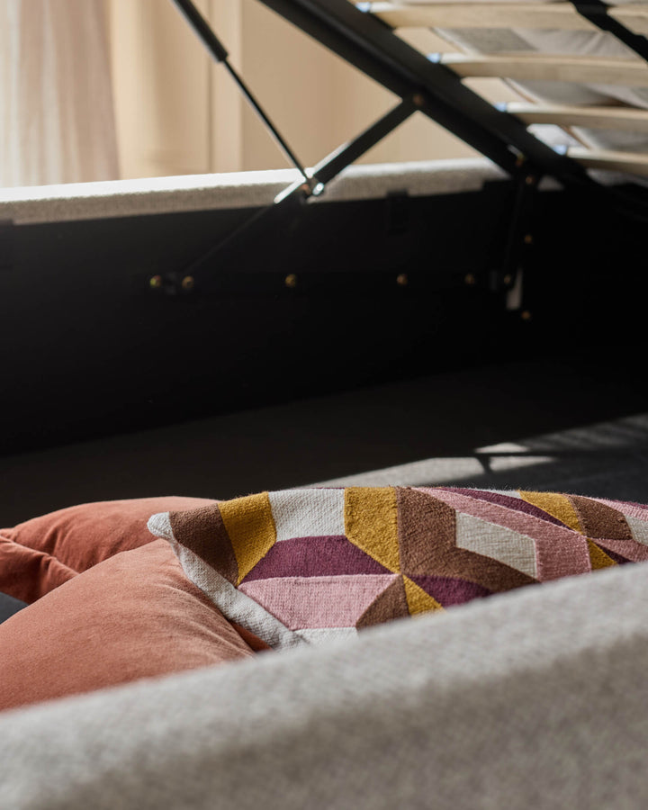 An ottoman storage bed with brown and patterned cushions. Ideal for space-saving, stylish bedroom furniture.