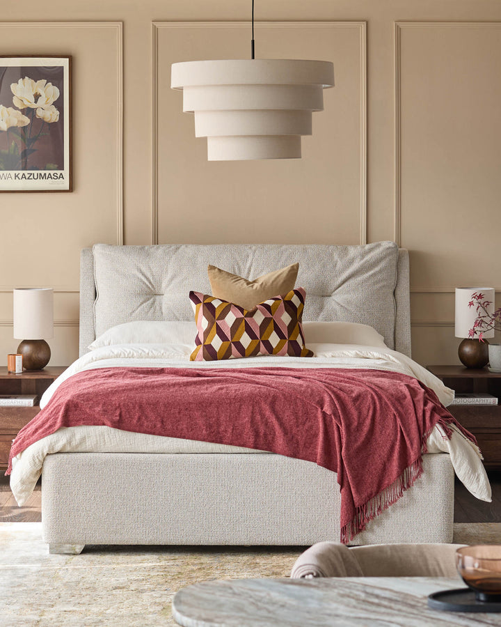 A stylish bedroom with a neutral upholstered bed, patterned cushions and a layered pendant light.