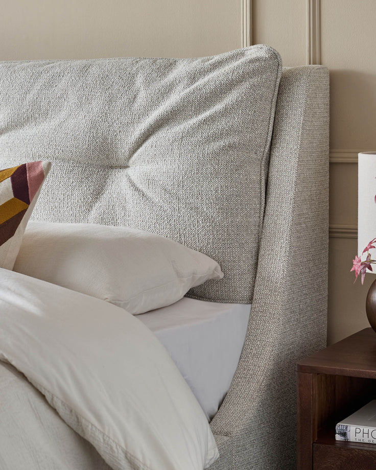 Beige upholstered super king-size ottoman bed with textured fabric headboard and white bedding, angled side view.