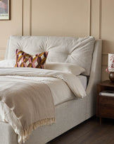 Upholstered bed with geometric cushion and throw, bedside table, and a modern, neutral colour scheme.