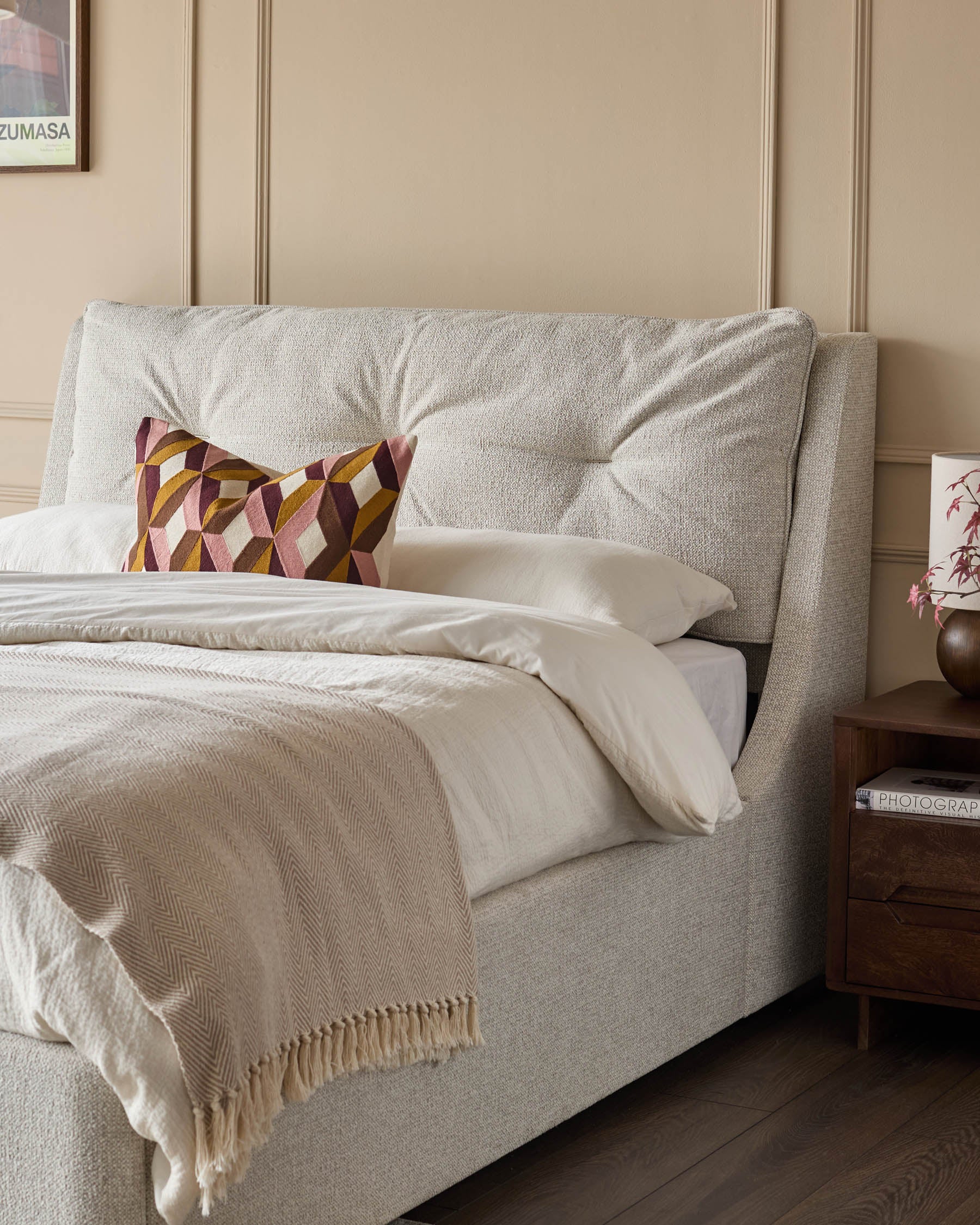 Upholstered bed with geometric cushion and throw, bedside table, and a modern, neutral colour scheme.