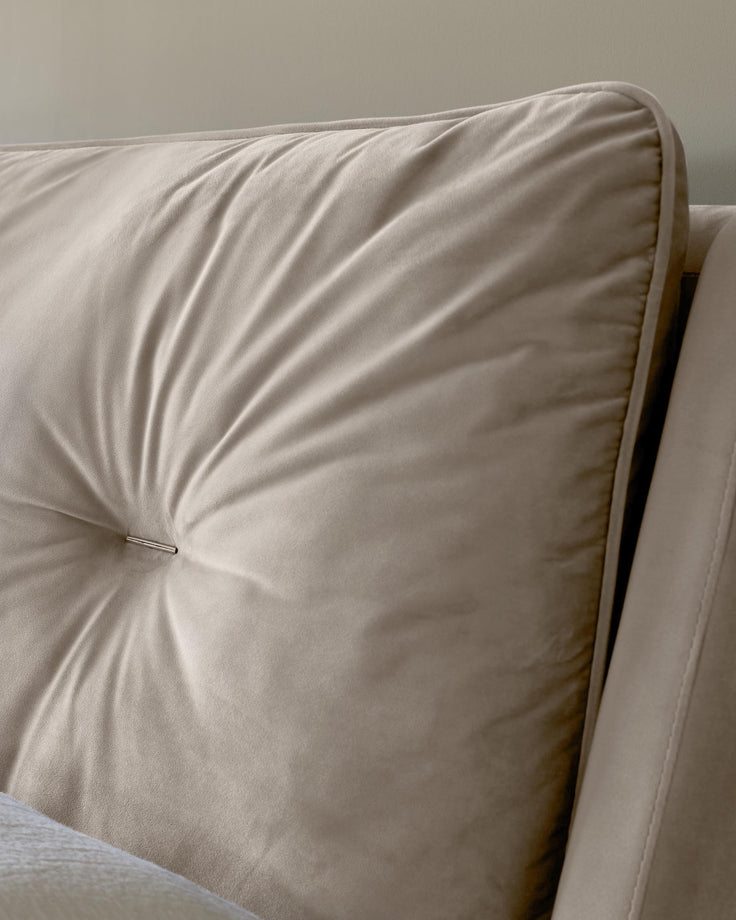 Close up of a beige cushion on a sofa, with a piped edge and a button in the centre.