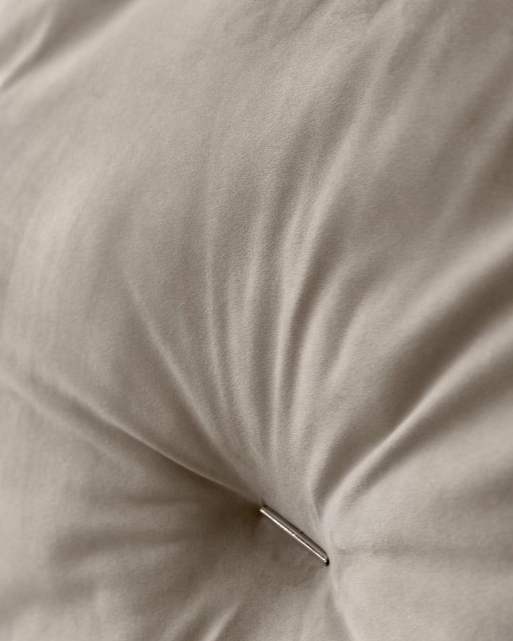 Close-up of a neutral coloured, buttoned cushion or mattress, showing the fabric texture and button detail.