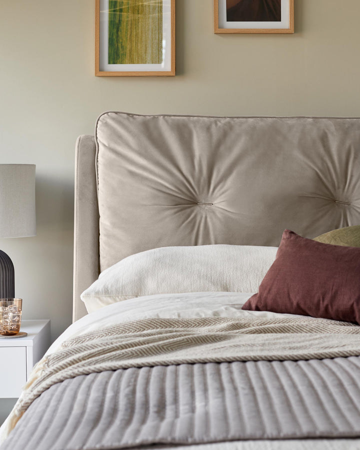 Bedroom with a button-back headboard, white bedding, and a bedside table with a lamp and a glass of water.