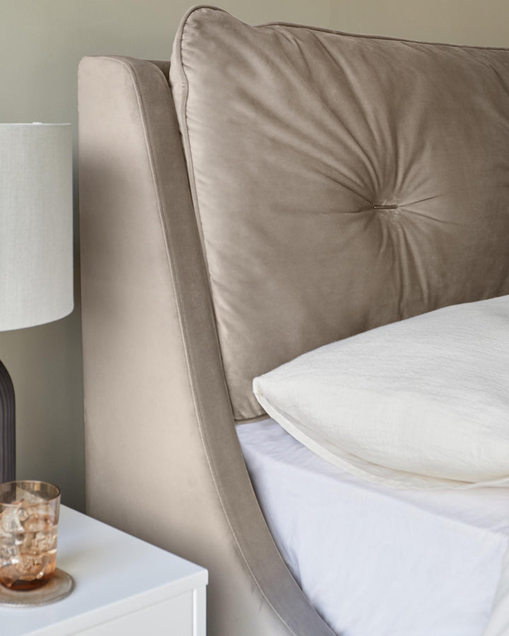 Champagne velvet super king bed with tufted headboard and white bedding, nightstand with glass visible.